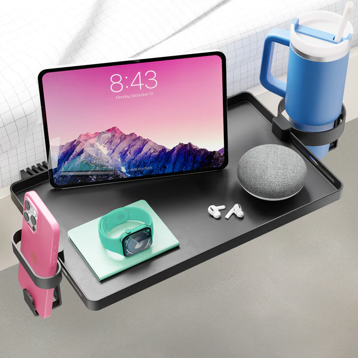 The DormEssential BedShelfie bedside shelf clamped to a dorm bunk bed, holding a tablet, phone, drink and earbuds